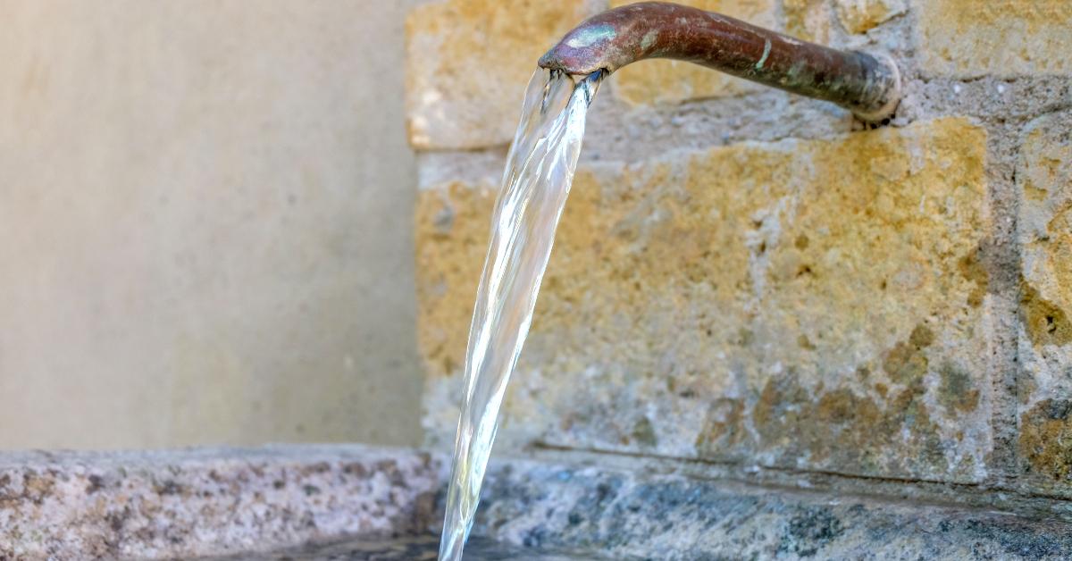 cold fresh water flows out of a metal tap in a rustic brick water basin