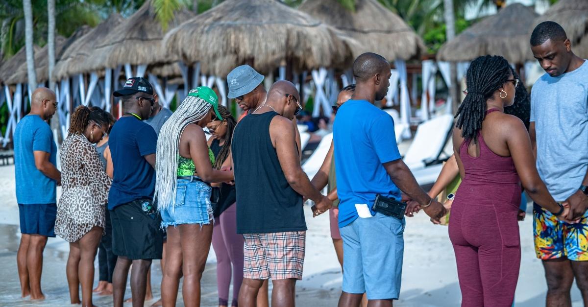 A group of Black couples hold hands on a beach.