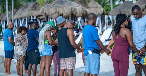 A group of Black couples hold hands on a beach.