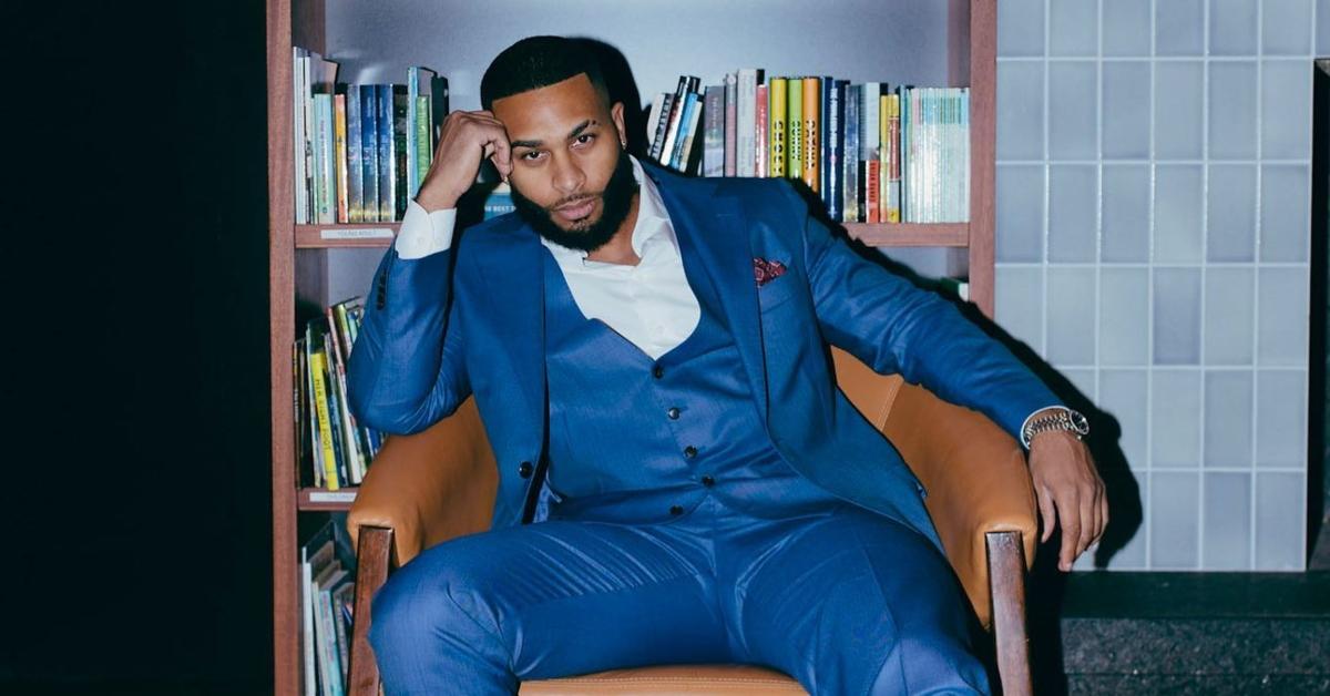 Ruben Harris sits in a chair in front of a bookshelf wearing a blue suit.