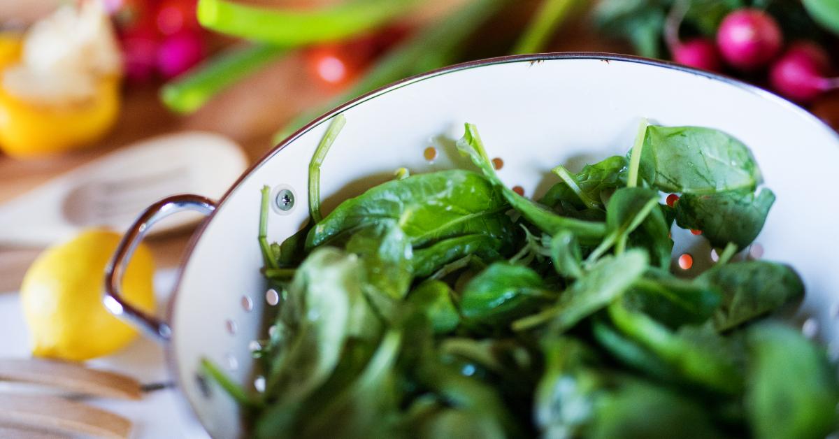 a bowl of fresh spinach on the table along with an assortment of vegetables