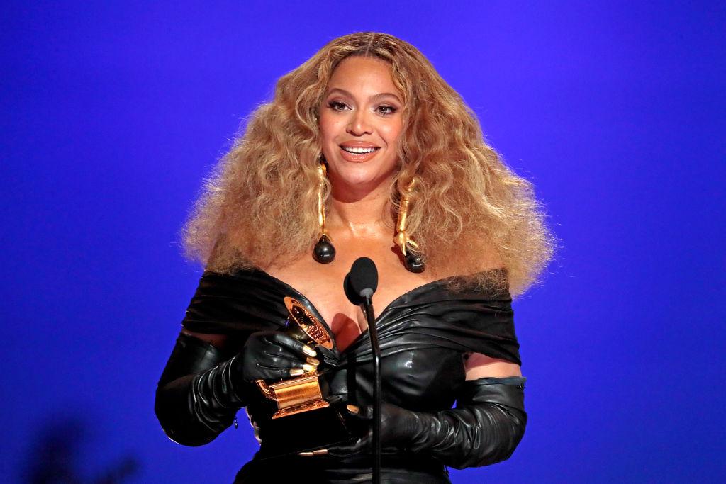 Beyonce wears a black off-the-shoulder dress while holding a Grammy Award.