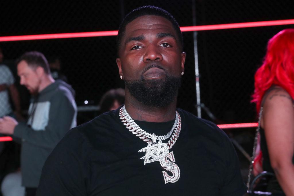 TSU Surf looks serious wearing a black shit and a large diamond chain that says RB.