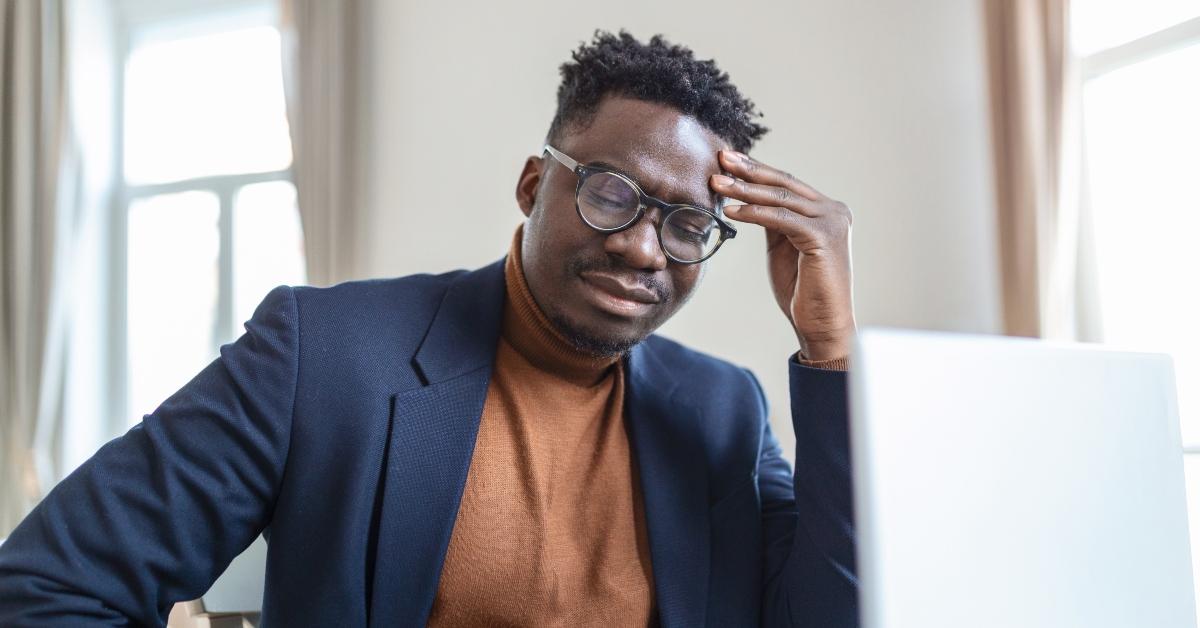 Black man dressed in business casual wear looks stressed out.