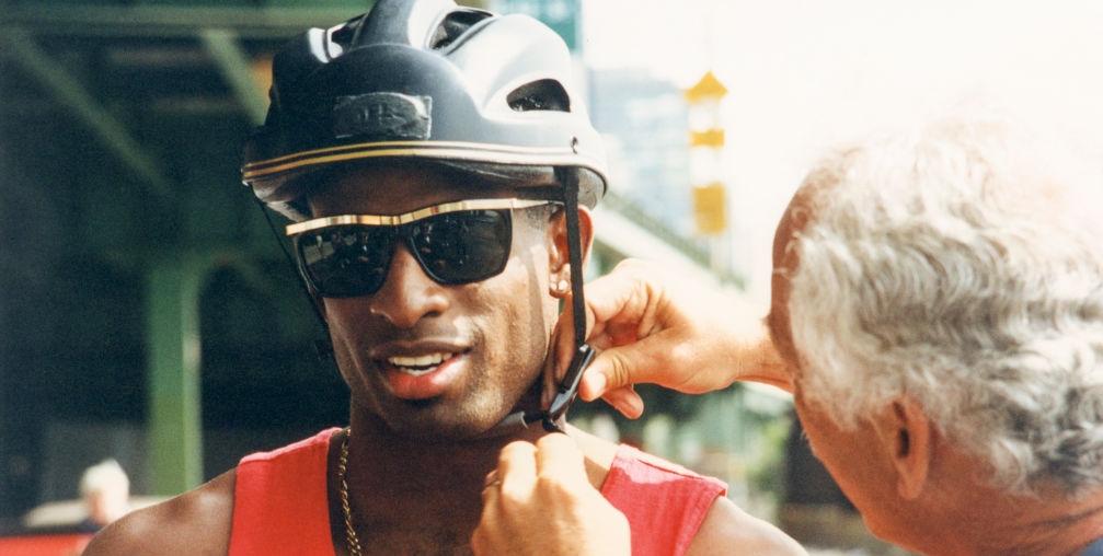 deion sanders has a bicycle helmet adjusted while wearing a red tank top