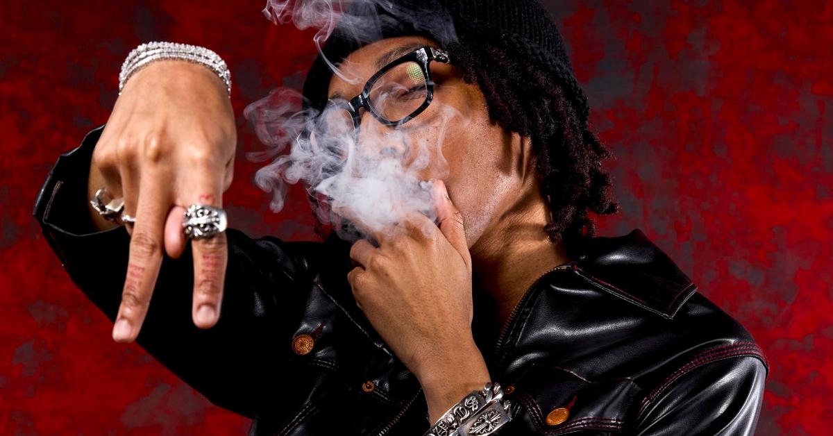Lil Tecca smoking in leather jacket with red background