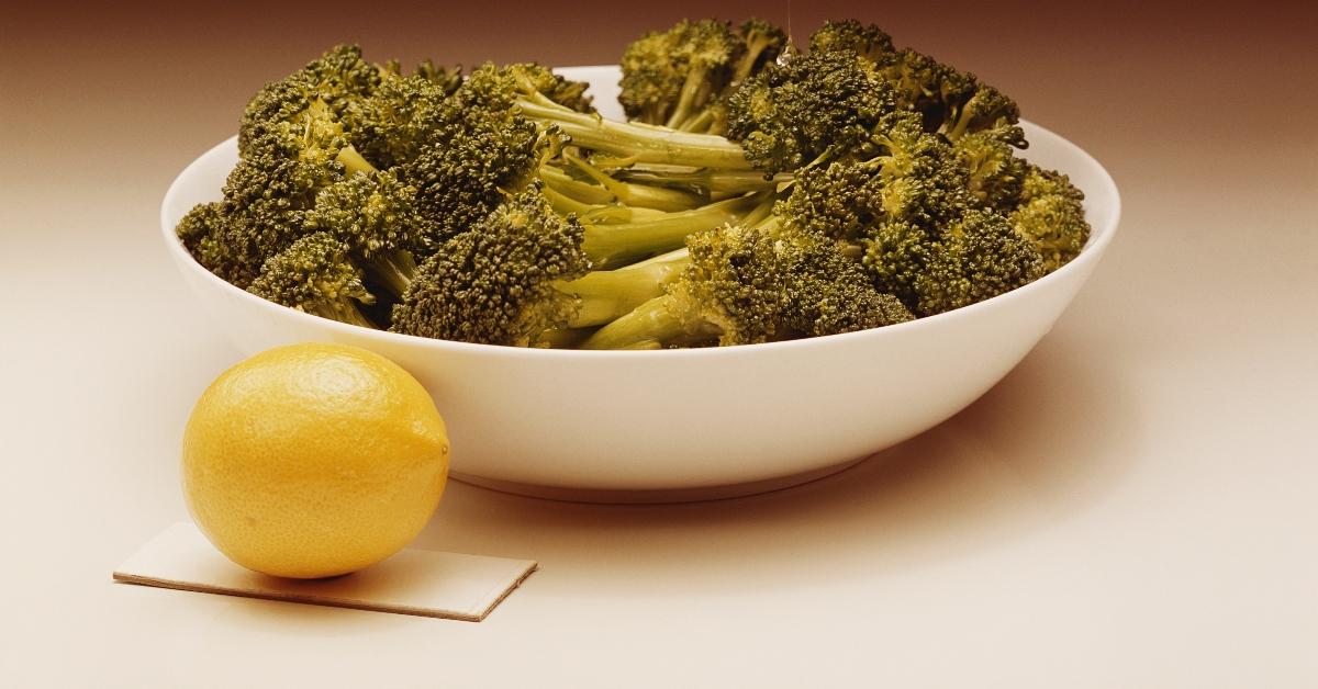 a bowl of fresh broccoli in a white bowl with a side of lemon