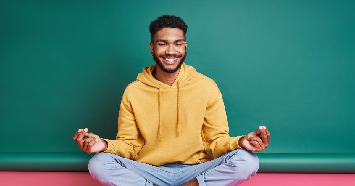 Happy Black man meditating while sitting against colorful background