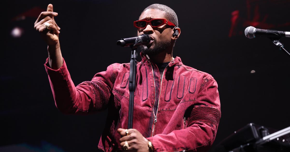 Usher performs on stage wearing red sunglasses and jacket.