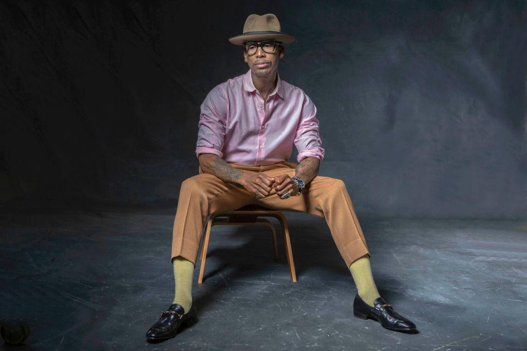 Producer, artist and legend, Raphael Saadiq wearing a pink button down shirt, orange pants, yellow socks and black shoes poses for a portrait in Both Hollywood, California