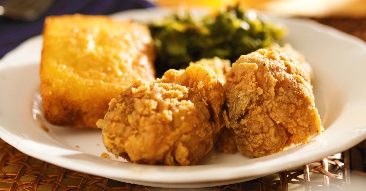 Cornbread, fried chicken, and greens plated on a white plate on a wicker table.