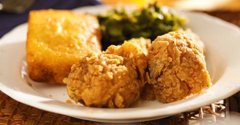 Cornbread, fried chicken, and greens plated on a white plate on a wicker table.