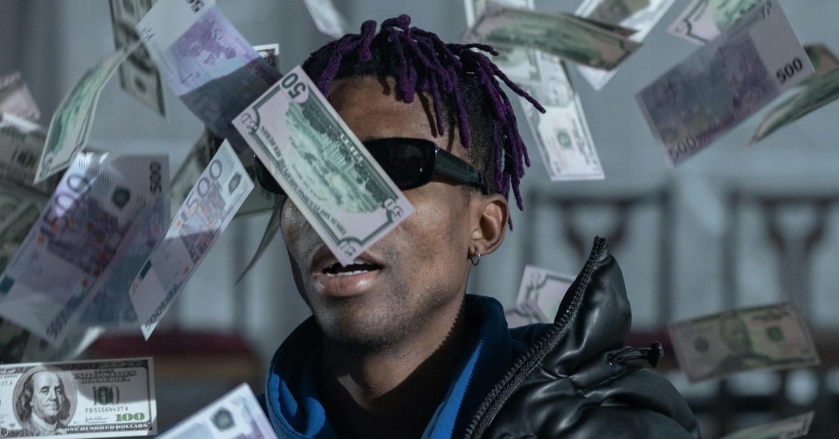 Money falls around a young Black man wearing sunglasses.