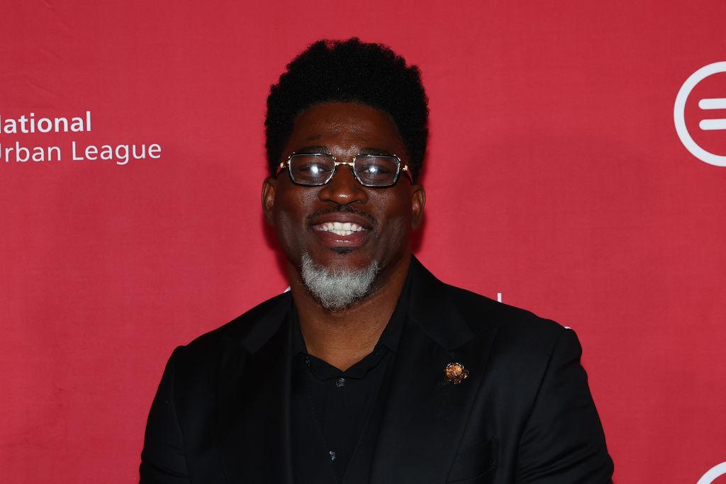 David Banner smiles and wears a black suit and black-brimmed glasses at a National Urban League event.