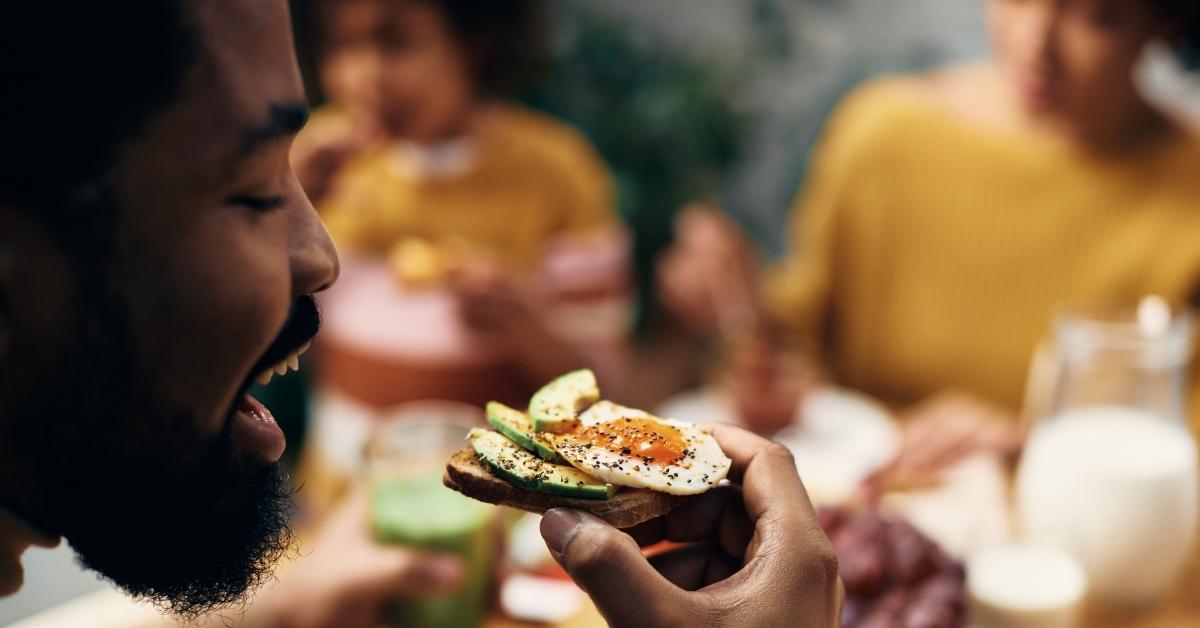 man eating avocado toast wiith egg at a table with friends