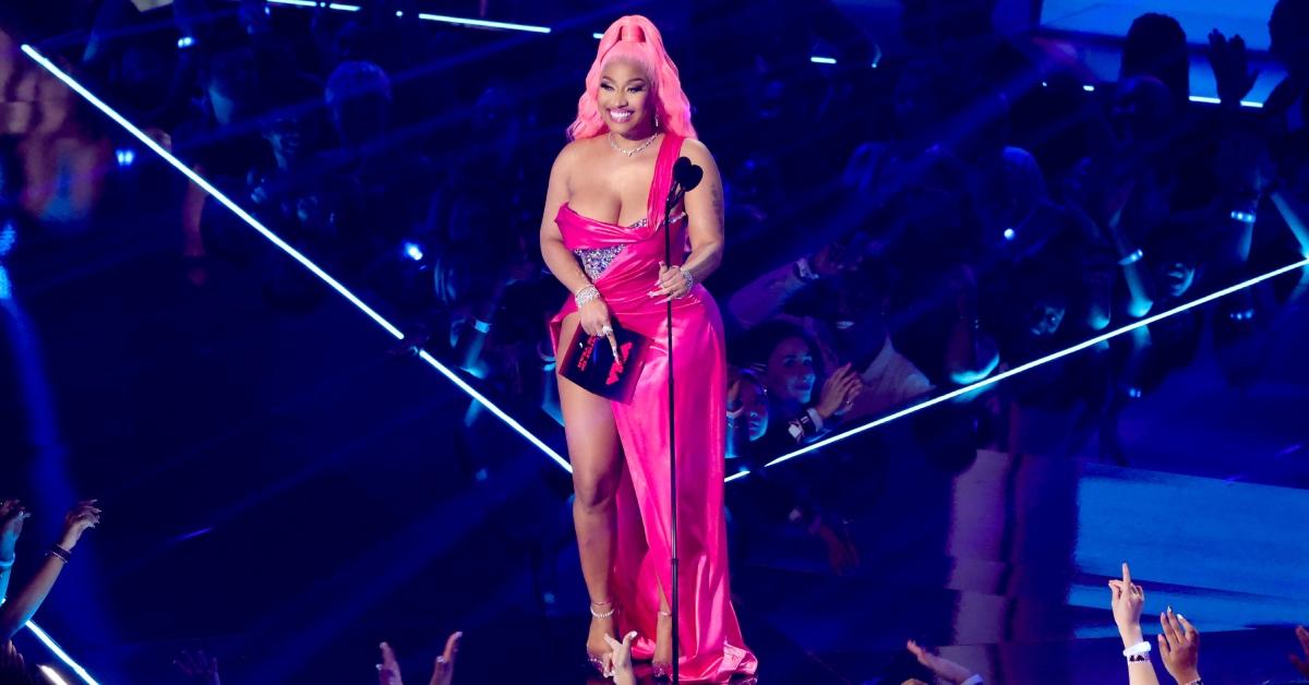 Nicki Minaj speaks in a bright pink dress onstage at the 2022 MTV VMAs at Prudential Center