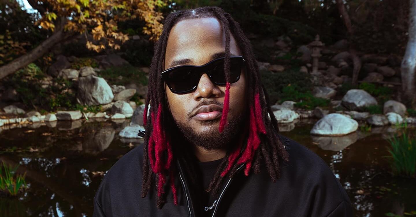 Leon Thomas wears sunglasses near trees with red hair