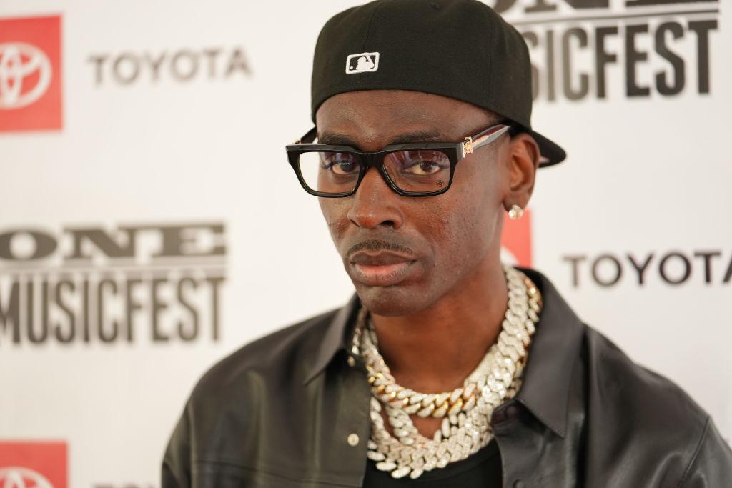 Young Dolph wears black sunglasses, black leather jacket, and gold chains on One Music Fest red carpet.