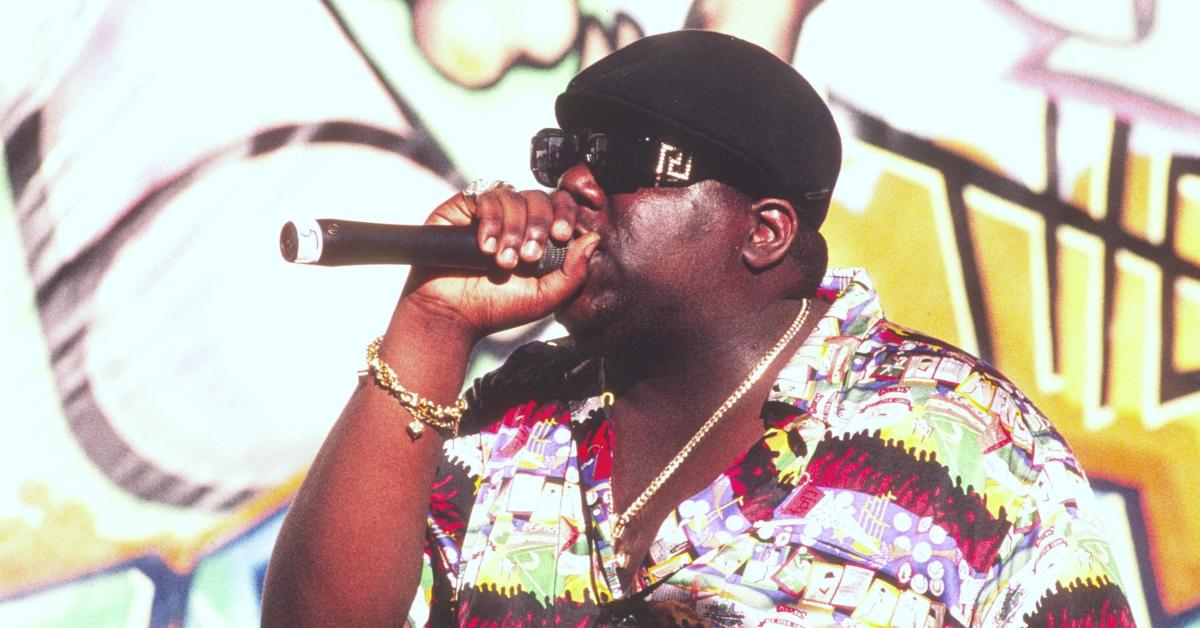 Biggie Smalls wears a colorful shirt and raps on stage.