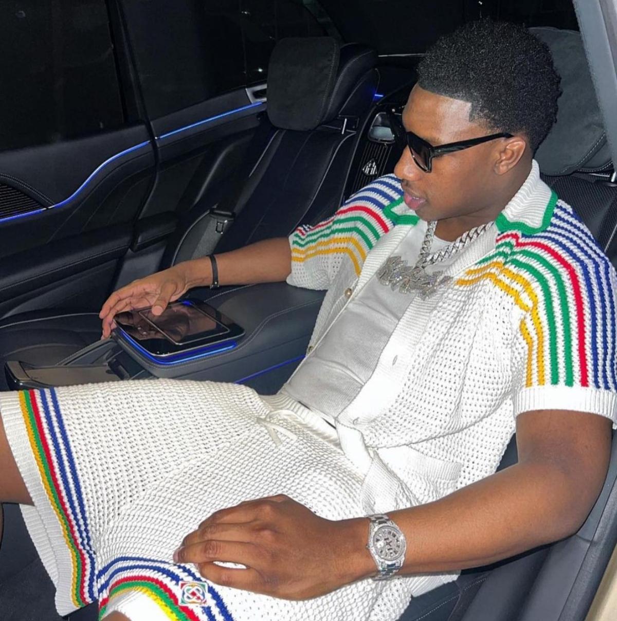 Rob49 wears crochet white blue red green and yellow outfit with diamond chain while he sits in the car.