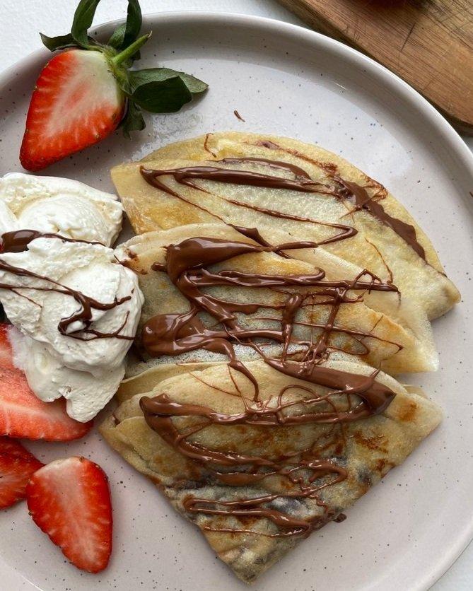 Vegan hazelnut chocolate crepes are plated and topped with berries and whipped cream