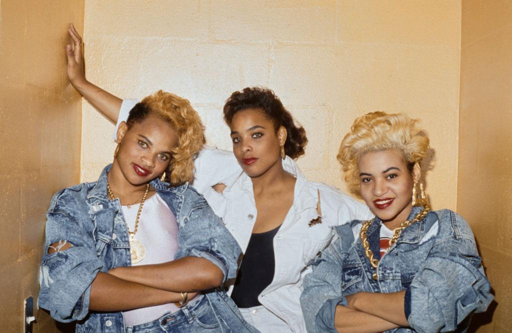 American hip hop band Salt-n-Pepa (Jamaican-American rapper Pepa, American DJ Spinderella, and American rapper Salt), with Pepa and Salt wearing denim jackets with their arms folded, in a studio portrait, United States, circa 1990.