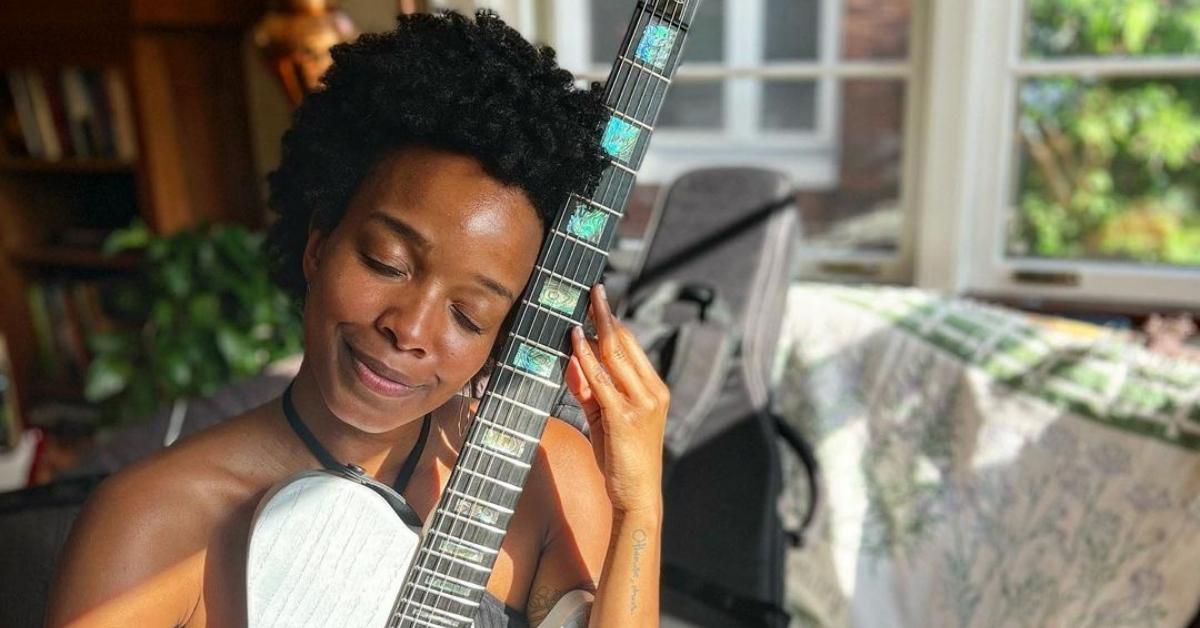 Jamila Woods cradles a guitar with her eyes closed in a living room.