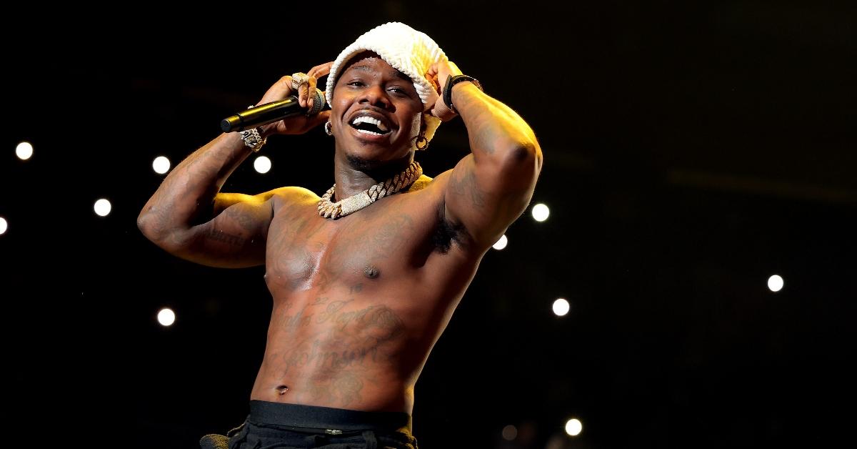 DaBaby is shirtless smiling at the crowd while preforming