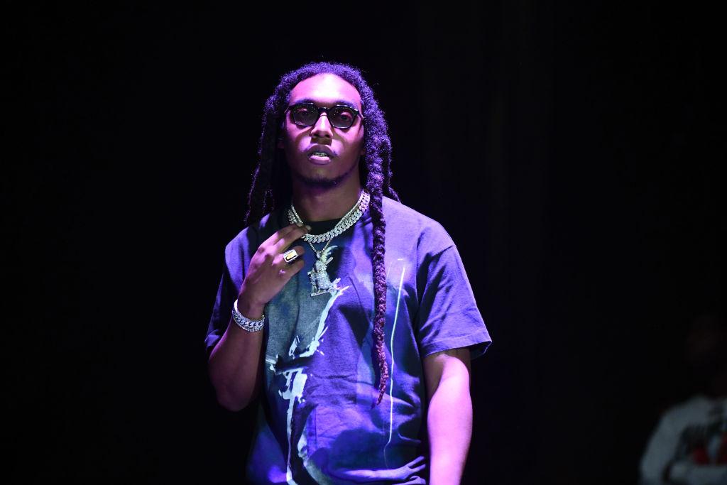 Takeoff from the migos wears glasses and a diamond chain on stage.