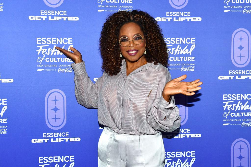 Oprah Winfrey smiles of the red carpet of Essence Festival's Get lifted event in striped button down and white linen pants.