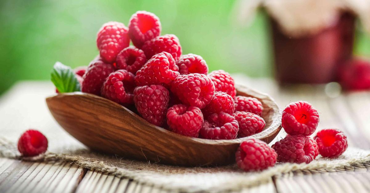 a pile of raspberries in a bowl on a wooden table outside