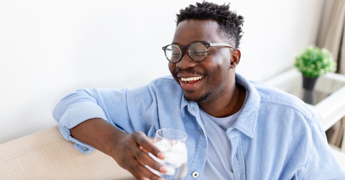 black man blue shirt smiles drinking a glass of water