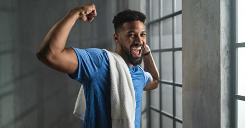 A young black man wearing a blue shirt flexes his muscles in the gym.