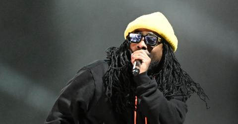 Wale performs on stage wearing a black jacket and a beanie.