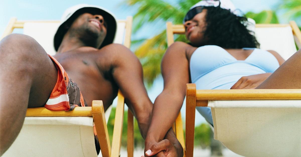 couple sitting on deck chairs holding hands on the beach